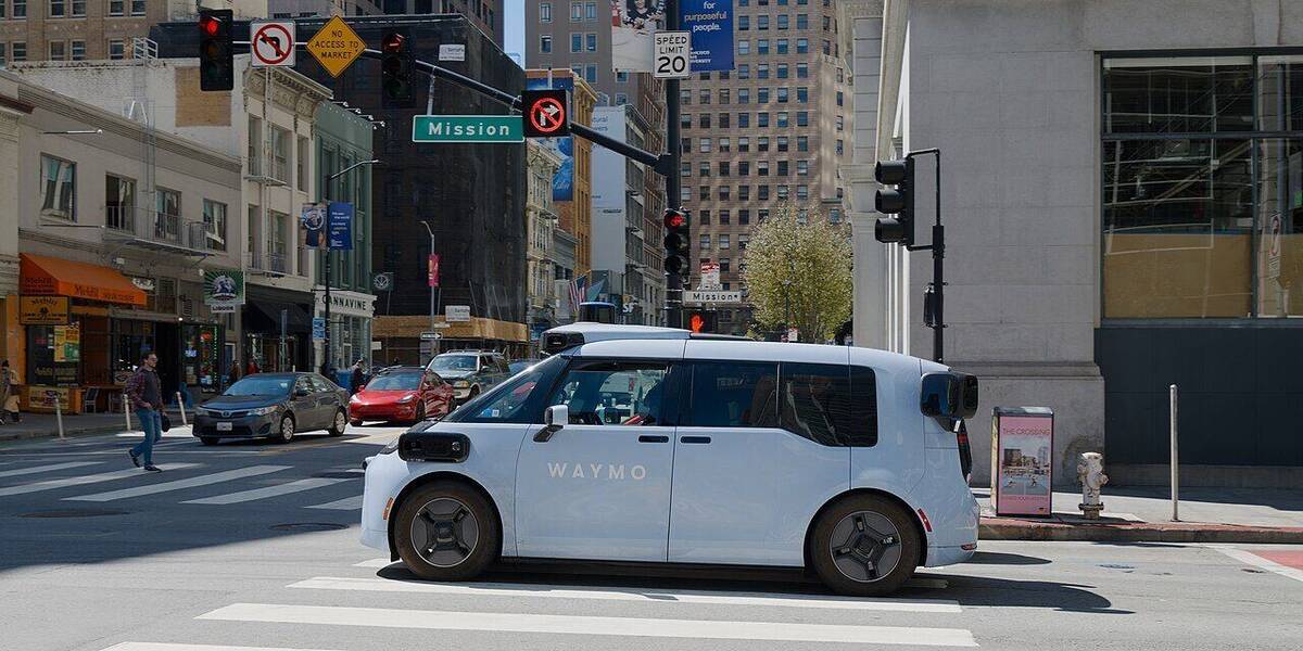 A white Waymo robotaxi on a city street at a crosswalk.