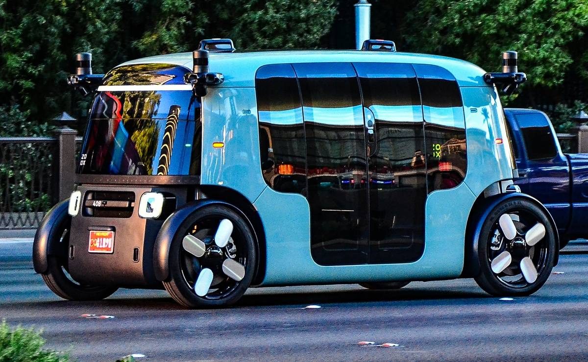 A light-blue Zoox robotaxi with no steering wheel on a city street.